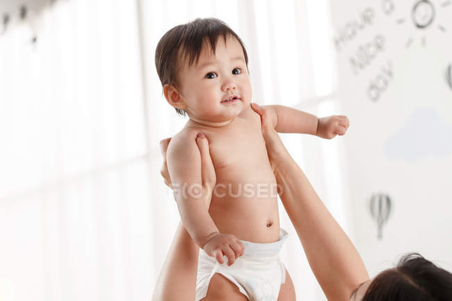 Schnappschuss von junger Mutter, die entzückendes asiatisches Baby in Windel zu Hause trägt — Stockfoto