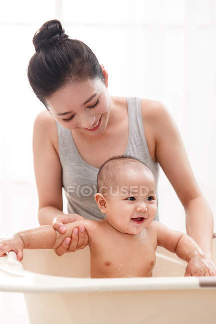 Happy young mother bathing adorable infant child in bathtub — Stock Photo