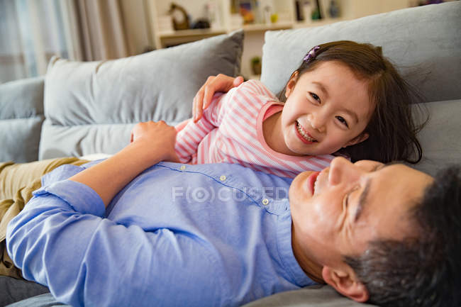 Happy asian father and cute little daughter playing and having fun together on couch — Stock Photo