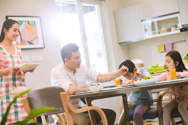 Família chinesa feliz com duas crianças comendo juntas em casa — Fotografia de Stock