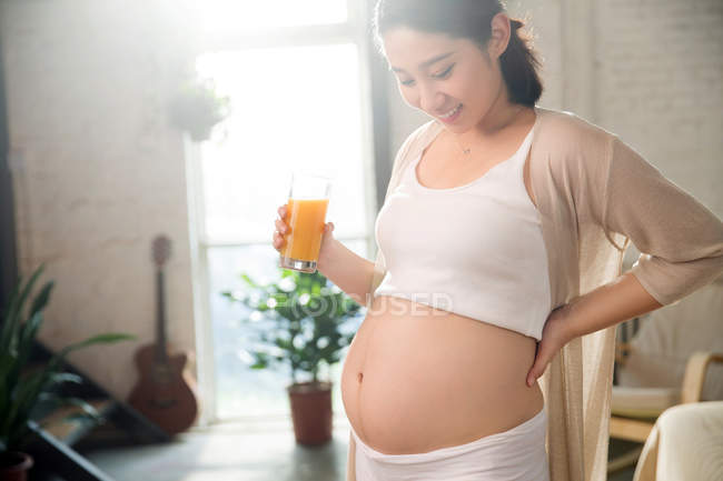 Sorrindo jovem grávida segurando vidro de suco fresco em casa — Fotografia de Stock