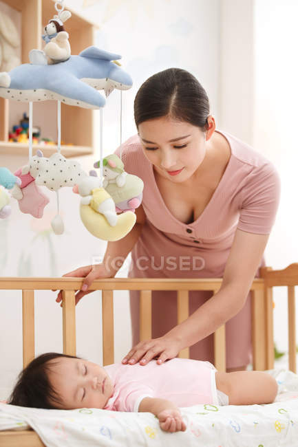 Счастливая молодая мать смотрит на очаровательный ребенок спит в кроватке — стоковое фото