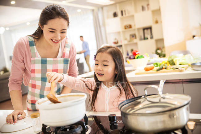 Красивая счастливая молодая мать с восхитительной маленькой дочкой готовят вместе на кухне — стоковое фото