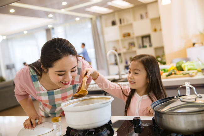 Hermosa feliz joven madre con adorable pequeña hija cocinar juntos en la cocina - foto de stock