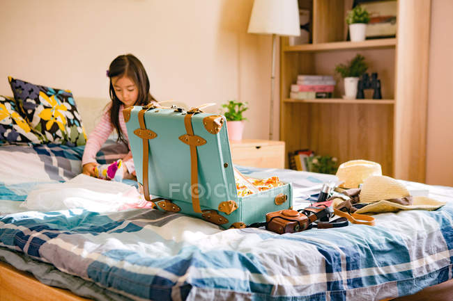 Cute little asian girl packing suitcase on bed — Stock Photo