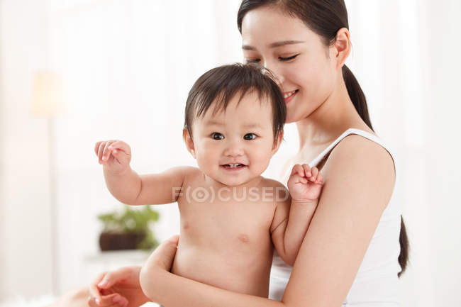 Happy young mother carrying adorable smiling baby at home — Stock Photo