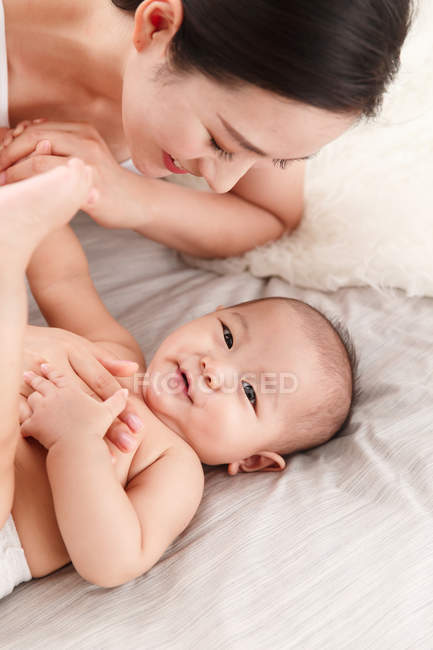 Alto angolo vista di felice giovane asiatica madre e adorabile neonato sdraiato insieme sul letto — Foto stock