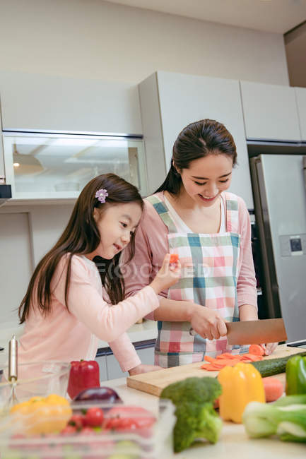 Happy young asian mother and adorable little daughter cooking together in kitchen — Stock Photo