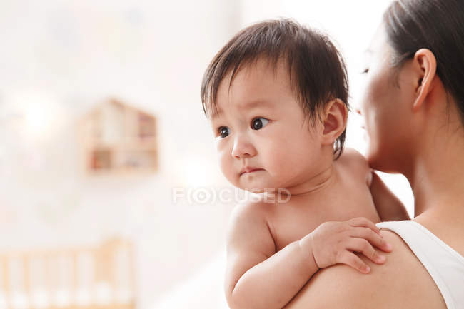 Tiro cortado de jovem mãe carregando adorável criança em casa — Fotografia de Stock