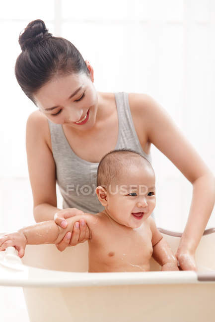 Happy yougn asian woman bathing her adorable baby in bathtub — Stock Photo