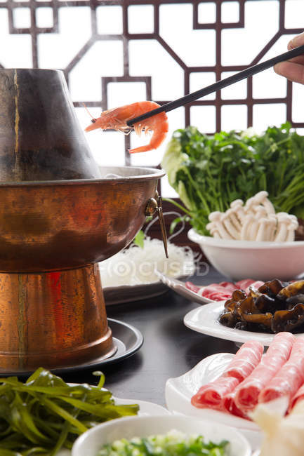 Cropped shot of person holding chopsticks with shrimp abuse copper hot pot, chafing dish concept — Stock Photo