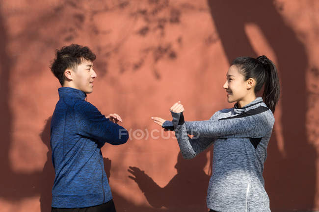 Vista lateral do jovem casal desportivo alongamento e sorrindo uns aos outros ao ar livre — Fotografia de Stock