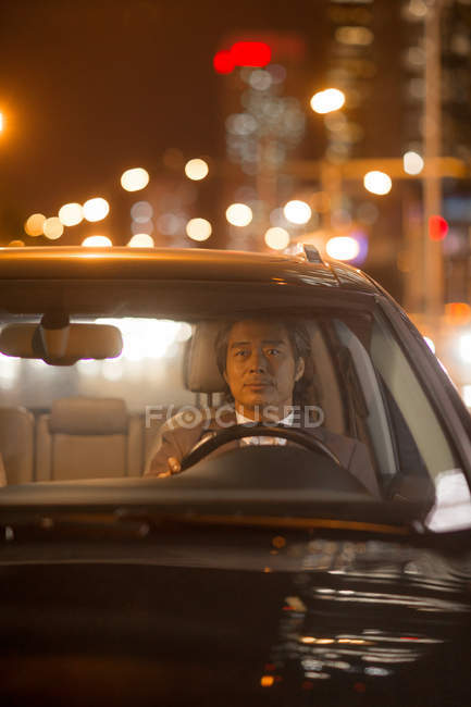 Вид через лобовое стекло серьезного зрелого мужчины, управляющего автомобилем в ночное время — стоковое фото