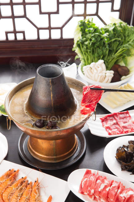 Vista de cerca de palillos con carne por encima de la olla caliente de cobre, concepto de plato de roce - foto de stock