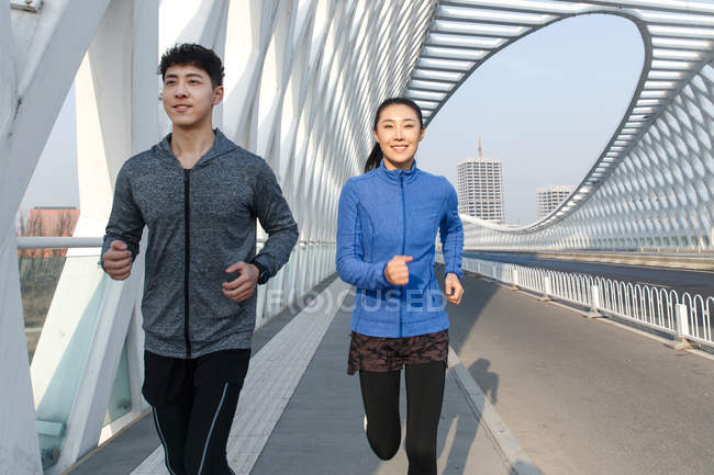 Smiling young male and female athletes running on bridge — Stock Photo