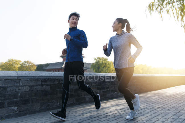 Низкий угол обзора молодой азиатской пары в спортивной одежде, улыбающейся друг другу и бегающей вместе утром — стоковое фото