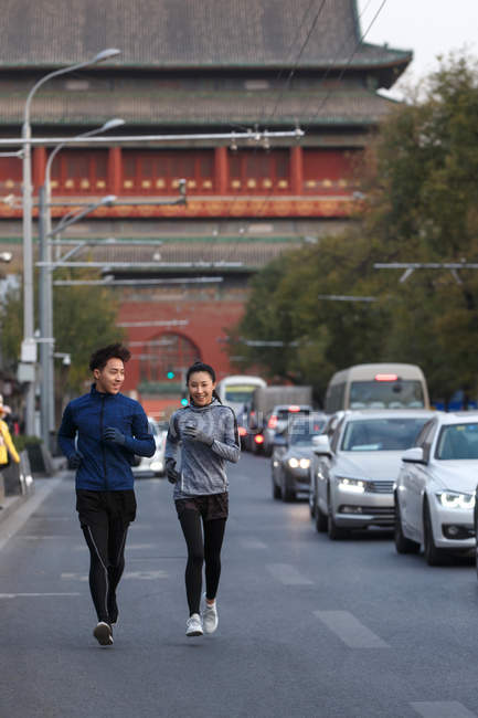 Vista frontal de la joven pareja deportiva sonriendo y corriendo juntos en la calle - foto de stock