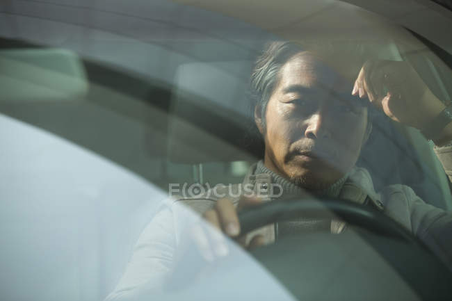Серьезный зрелый азиатский мужчина сидит в машине и смотрит в камеру — стоковое фото