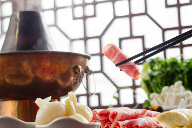 Vista de cerca de palillos con carne y olla caliente de cobre, concepto de plato de roce - foto de stock