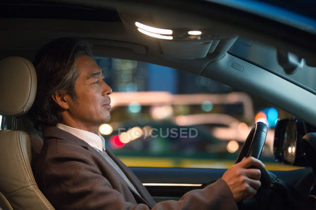 Side view of serious mature asian businessman driving car at night — Stock Photo
