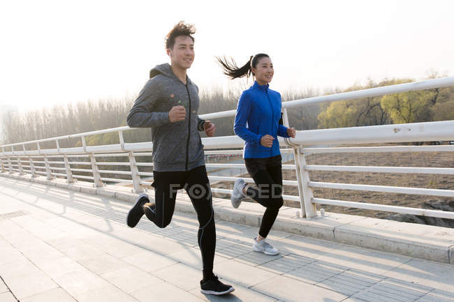 Sorrindo jovem asiático homem e mulher correndo juntos na ponte — Fotografia de Stock