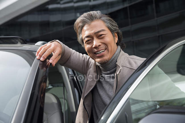 Bonito feliz ásia homem de pé perto de carro e sorrindo para câmera — Fotografia de Stock