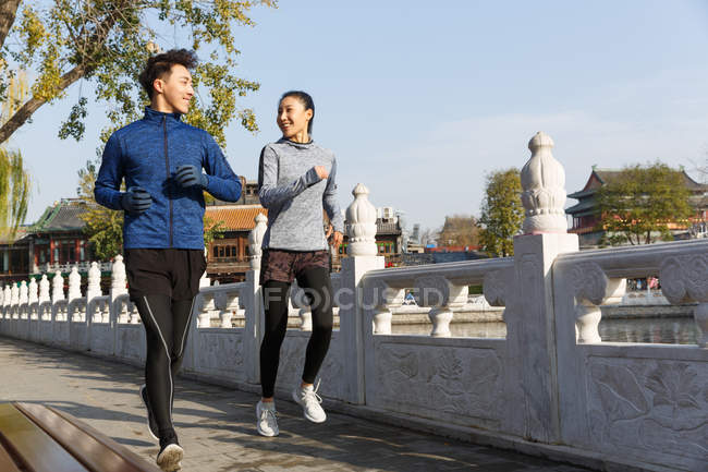 Sportliches junges Paar lächelt einander an und läuft gemeinsam auf der Straße — Stockfoto