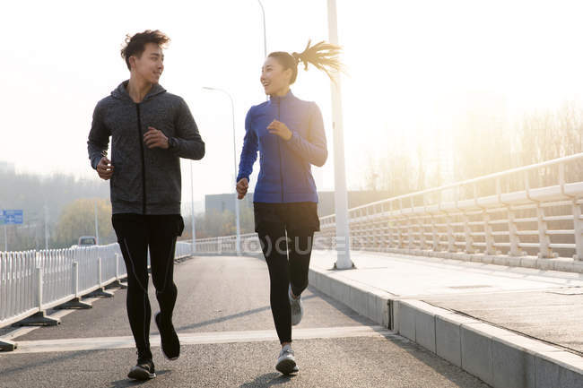 Feliz jovem asiático casal no sportswear sorrindo uns aos outros e correndo juntos ao ar livre — Fotografia de Stock