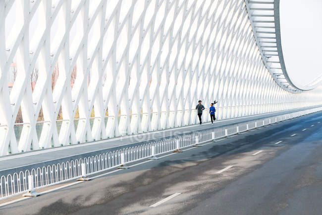 Ganzkörperansicht junger Sportler und Sportlerin, die gemeinsam auf moderner Brücke laufen — Stockfoto