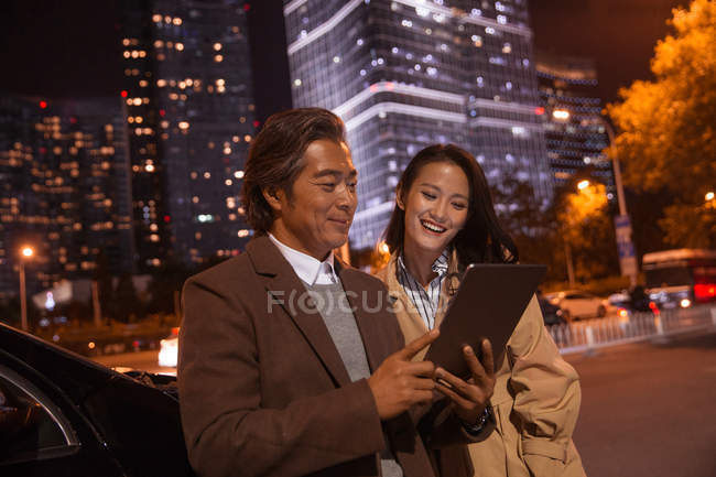 Happy asian couple looking at tablet near car at evening — Stock Photo