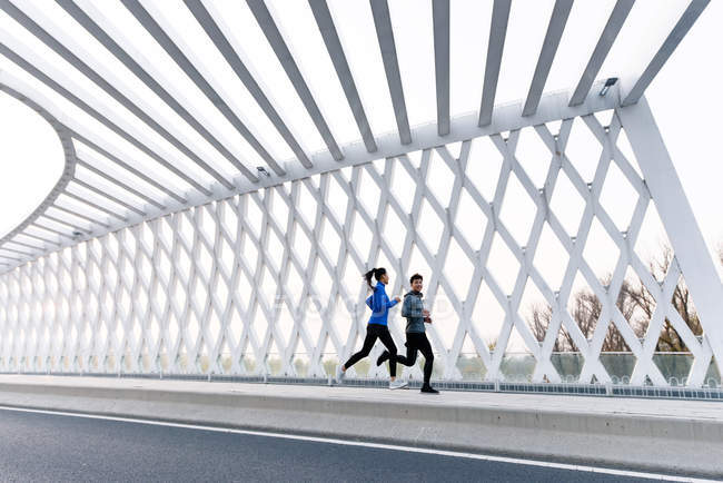 Повний вигляд молодої азіатської пари, що біжить разом на мосту — стокове фото