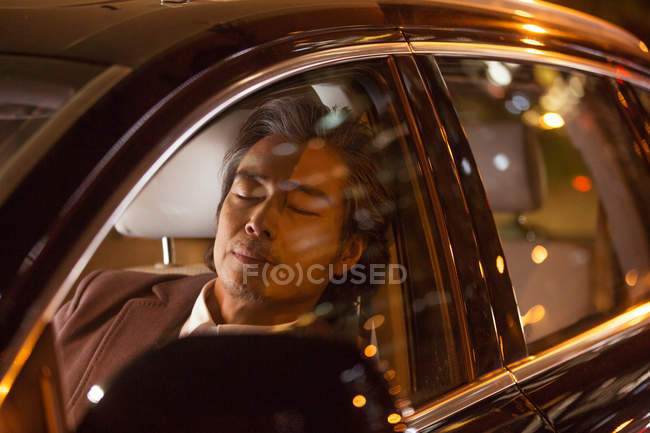 Tired mature asian man sleeping in car at night — Stock Photo