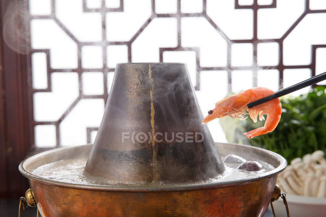 Vista de cerca de palillos con camarones por encima de la olla caliente de cobre, concepto de plato de roce - foto de stock