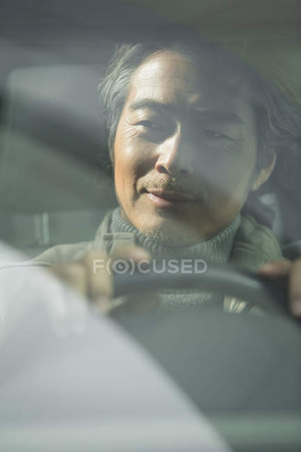 Вид через вітрове скло усміхненого азіатського чоловіка, що водить машину — стокове фото