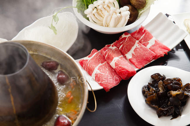 Vista ravvicinata di pentola di rame calda, carne e funghi sul concetto piatto di sfregamento tavolo — Foto stock