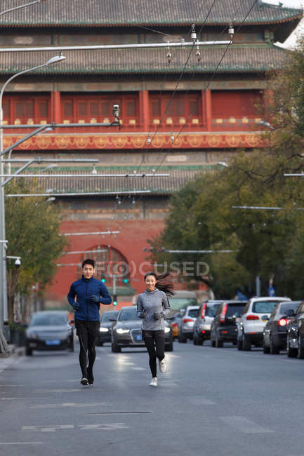 Longitud completa vista de sonriente joven asiático joggers formación juntos en calle - foto de stock