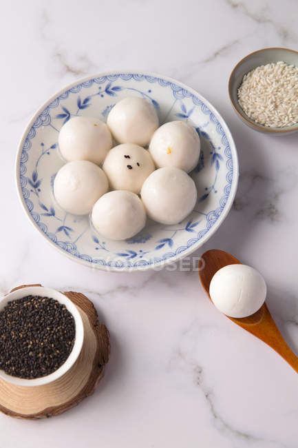 Boules de riz gluantes sur assiette, cuillère en bois et bols avec graines de sésame sur la table, vue sur le dessus — Photo de stock