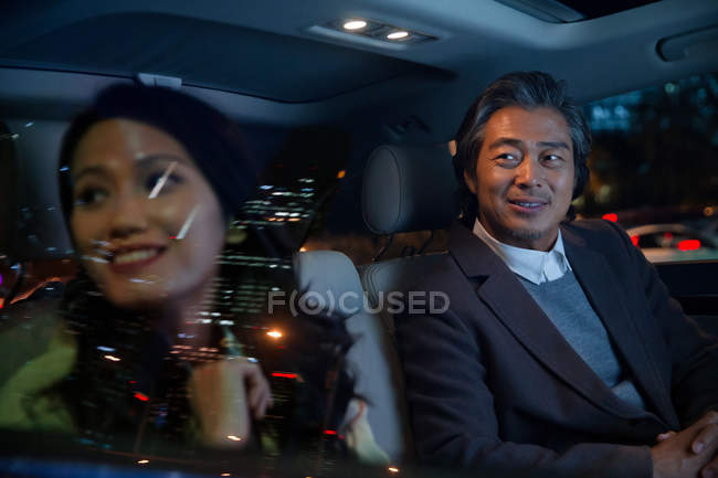 Happy asian couple riding in car and looking out of window at evening — Stock Photo
