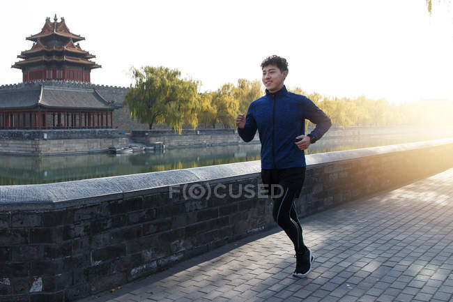 Повний вигляд усміхненого молодого азіатського чоловіка, що біжить на відкритому повітрі вранці — стокове фото