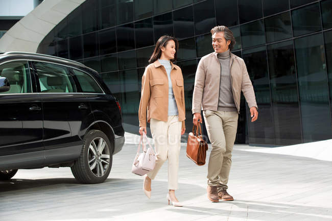 Cheerful asian businesspeople walking near parking at modern business center — Stock Photo
