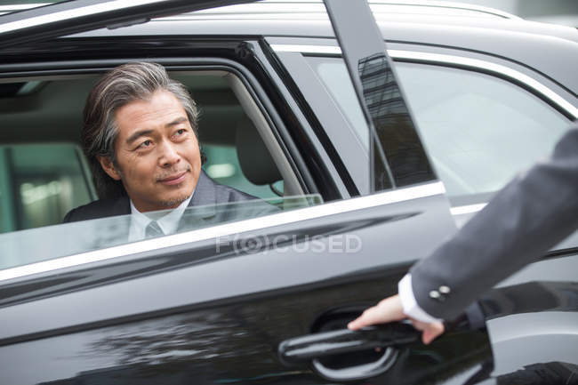 Обрезанный снимок того, как кто-то открывает дверь машины для улыбающегося взрослого бизнесмена — стоковое фото