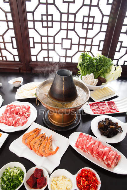 Olla caliente de cobre, verduras, carne y mariscos en la mesa, concepto de plato de roce - foto de stock