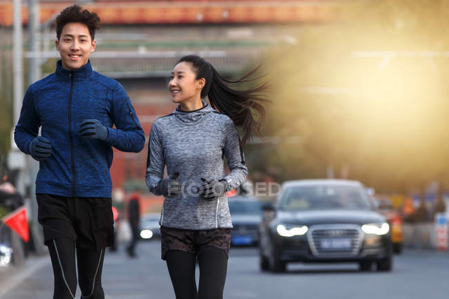 Sonriente joven asiático sportswoman mirando novio mientras corriendo juntos en calle - foto de stock