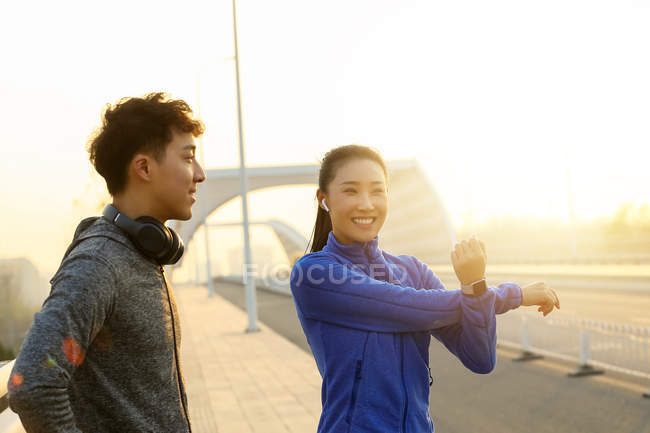 Young asian man and woman in sportswear stretching during workout on bridge in the morning — Stock Photo