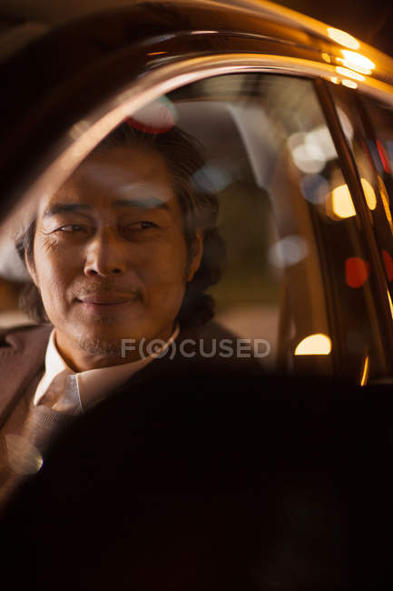 Крупным планом улыбающийся взрослый азиатский мужчина за рулем автомобиля, избирательный фокус — стоковое фото