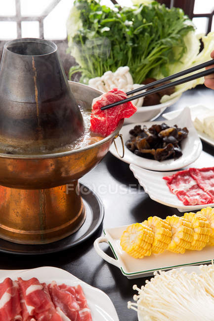 Cropped shot of hand holding chopsticks with meat above copper hot pot, chafing dish concept — Stock Photo