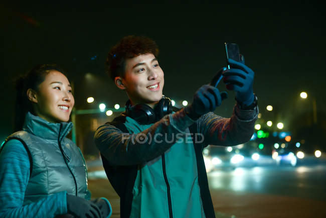 Felice sportivo giovane coppia asiatica prendendo selfie con smartphone durante l'allenamento di notte — Foto stock