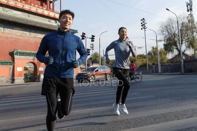 Спортивна молода усміхнена азіатська пара біжить разом на вулиці — стокове фото