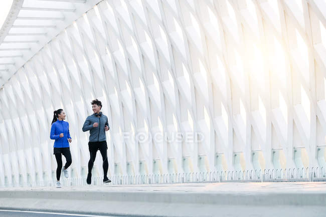 Спортивная молодая азиатская пара улыбается друг другу и бегает вместе по мосту — стоковое фото