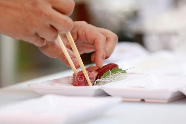 Abgeschnittene Aufnahme einer Person, die Essstäbchen hält und Thunfisch isst — Stockfoto